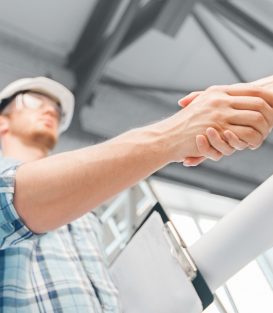 architecture and home renovation concept - builder with blueprint shaking partner hand